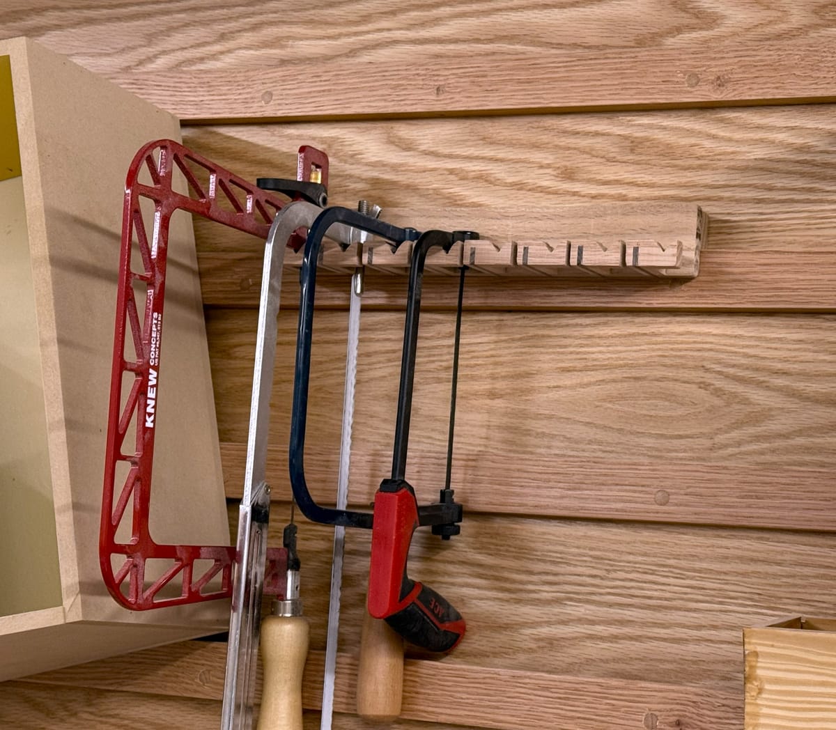 Small wooden arms holding up hand saws on a wood wall