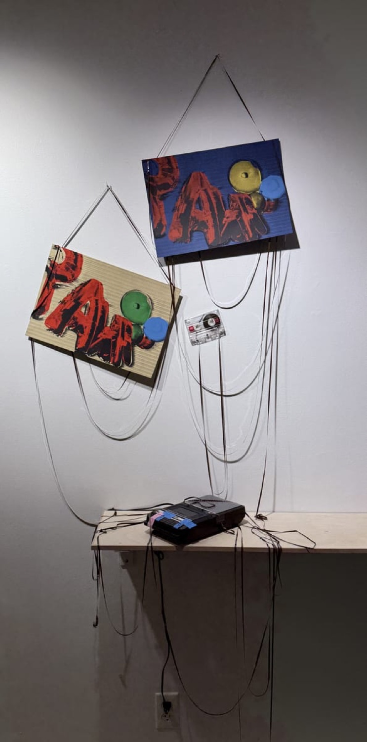 Gallery installation: prints hung by tangled cassette tape with a cassette player